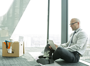 Dieses Bild zeigt einen Geschäftsmann, der auf dem Boden eines leeren Büros sitzt und mit einem Laptop arbeitet (© Westend61)